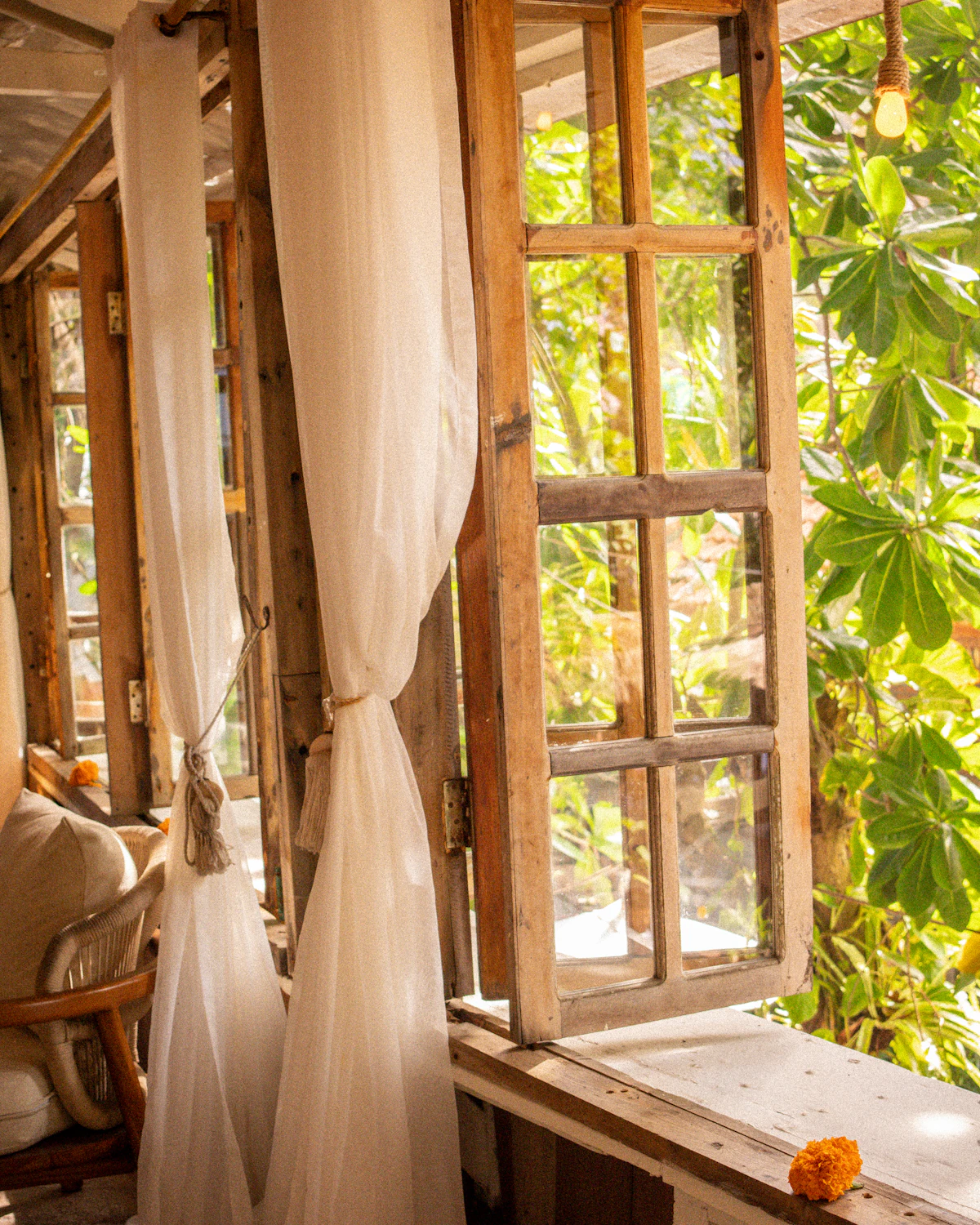 A teak four-poster bed under a linen canopy in an open-sided villa, facing the sea at dawn.